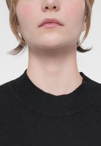 Black sweater featuring a ribbed crew neck design, smooth texture, and a fitted silhouette, seen from the collar up with minimal background.