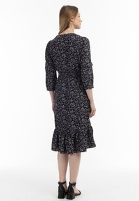 Rochie neagră cu flori, cu mâneci trei sferturi, bază cu volane și talie elastică. Prezintă modele mici de flori roz și albe pe întreaga suprafață.