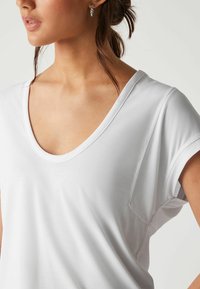 Witte korte mouw V-hals t-shirt gemaakt van een zachte, gladde stof, met een subtiele zakdetail aan de linkerkant.