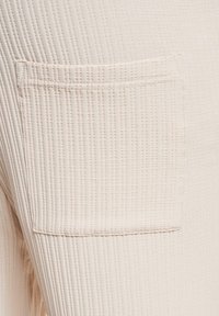 Lys beige stof med et struktureret ribbet mønster. Har en lappelomme, der er syet pænt på den øverste side.
