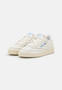 Witte leren sneakers met lichtgrijze accenten, platte veters en een gestructureerde zool. Bevat een blauw logo aan de zijkant en een zachte binnenvoering.