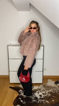 Rozā mākslīgās kažokādas īsie apģērba izstrādājumi, melni bikses un sarkana spīdīga somiņa. Modelis nēsā tumšas saulesbrilles. Redzami gludi audumi un kontrastējošas krāsas.