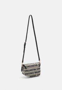 Přes rameno taška ze šedé látky s černým logem. Obsahuje klopu přes horní část, nastavitelný popruh a zlaté kovové doplňky.