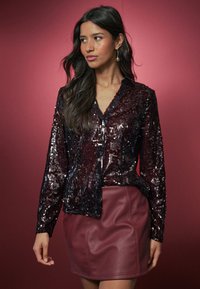 Burgundia värvi sädelev jakk šaali kraega, pikkade varrukate ja vormiva hemiga, mida on kombineeritud burgundia kunstnahast seelikuga.