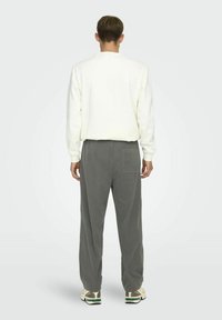 White sweatshirt, gray corduroy pants with back pocket, relaxed fit, and textured fabric. Model shown from the back with neutral background.