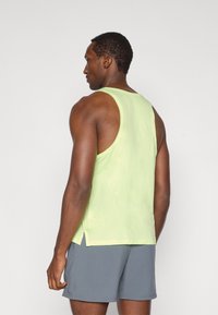 Ανοιχτό πράσινο αμάνικο αθλητικό τοπ με άνετη εφαρμογή και σχισμές στα πλάγια, κατασκευασμένο από διαπνέον υλικό. Φορεμένο με γκρι σορτς.