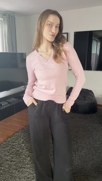 Light pink v-neck sweater with long sleeves, paired with loose-fitting black pants. Soft texture, relaxed fit, worn casually with hands in pockets.