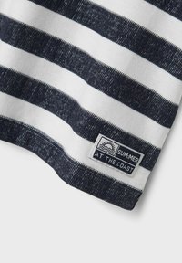 Camisa de algodón a rayas que presenta franjas horizontales alternas en azul marino y blanco. Incluye una etiqueta de logo con un diseño de sol y texto en el dobladillo.