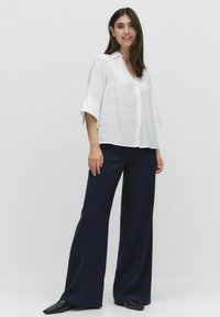 Hvid linned skjorte med krave og trekvartærmer, kombineret med mørke brede bukser. Outfitet har en afslappet pasform og minimalistisk design.