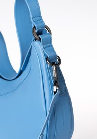 Lichtblauwe leren handtas met een gladde textuur, strak ontwerp en een zwart metalen hardware accenten op de riembevestiging.