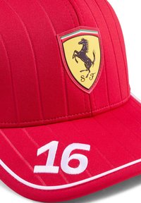 Rode pet met verticale strepen, voorzien van een gele Ferrari-logo patch en het nummer "16" geborduurd in het wit. Gemaakt van gestructureerd materiaal met een gebogen klep.