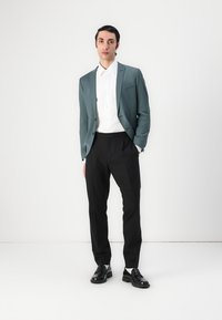 Blazer teal su misura sopra una camicia bianca con bottoni, abbinato a pantaloni neri e mocassini neri, caratterizzato da un design elegante e una texture liscia.