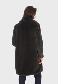 Manteau en fausse fourrure vert foncé avec une texture pelucheuse, manches longues et un col cranté, exposé de dos sur un fond neutre.