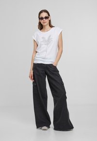 T-shirt blanc à manches courtes avec un motif de palmier, associé à un pantalon cargo noir large avec poches latérales et ourlets effilochés.