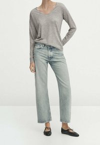 Pull gris à manches longues en V associé à un jean droit en denim clair et des ballerines noires. Tenue simple et décontractée avec peu de détails.