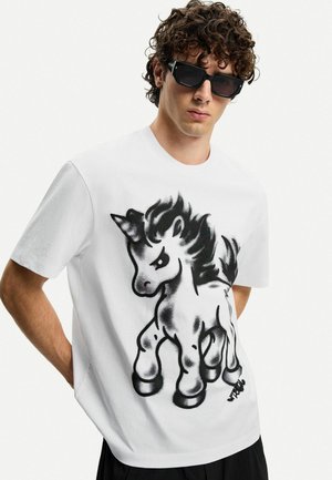 T-shirt bianca in cotone con una grafica di unicorno nera, maniche corte, colletto rotondo e una vestibilità rilassata. Stampa testurizzata che aggiunge dettaglio.