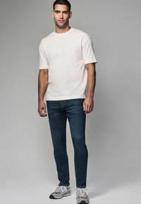 Hea helebeež särk lühikeste varrukatega, tume sinine teksapüksid ja hallid sneakersid valgete paeltega. Lihtne disain, tavaline lõige, ilma mustrite või dekoratsioonideta.