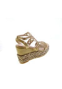 Scarpa con zeppa beige con suola in juta intrecciata. Parte superiore in camoscio con un design a intaglio intricato e accenti metallici sottili. Fascetta alla caviglia regolabile.