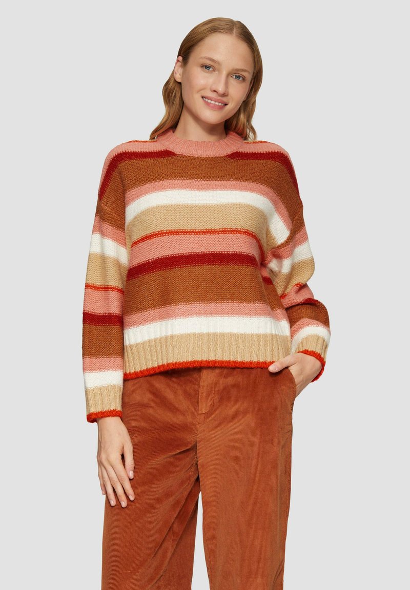 Gestreifter Pullover in warmen Tönen von Rot, Beige und Pink. Gefertigt aus einem strukturierten Strickstoff mit geripptem Saum und weit geschnittenen Ärmeln. Kombiniert mit Cordhosen.