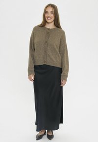 Hnědý vlněný cardigan s ribovanou strukturou a pěti knoflíky, spárovaný s dlouhou černou saténovou sukní a tmavými botami. Disponuje zkráceným střihem.