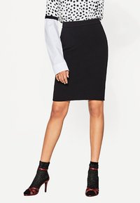 Zwarte kokerrok met een middellange ontwerp, gemaakt van rekbare stof. Combinatie met een blouse met stippen en zwarte gestructureerde sokken.