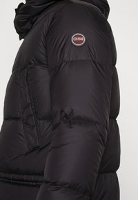 Svart puffjacka med kviltade sektioner, en framträdande COLMAR-logotyp på ärmen och en huva för extra värme och skydd.