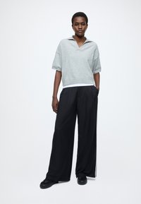 Siva polo majica kratkih rokavov je združena s črnimi širokimi hlačami z belimi stranskimi črtami in črnimi teksturiranimi supergami.