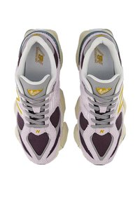 Zapatillas New Balance 9060. Malla púrpura con acentos de ante gris, logo amarillo y suelas gruesas color crema. Diseño con cordones y cuello acolchado.