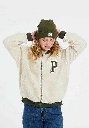 Krem žuti flis jakna sa zatvaranjem na zip i zelenim rebrastim manžetama, sa velikim izvezenim slovom "P" na grudima. Maslinasto zeleni beanie.