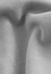 Tessuto grigio testurizzato con fini righe uniformi e una leggera lucentezza, che mostra pieghe e avvallamenti morbidi in una forma drappeggiata.