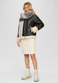 Veste en cuir noir avec des accents en fausse peau de mouton crème, associée à une écharpe texturée grise et blanche, une jupe crème et des bottines beige.