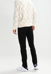 Maglione di peluche con motivo a rombi blu navy, abbinato a pantaloni slim-fit neri e sneaker bianche con accenti blu navy.