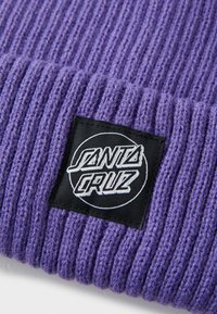 Lilla strikket behue med ribbet tekstur. Har en svart rektangulær lapp med et rundt logo som viser "SANTA CRUZ" i hvit tekst.