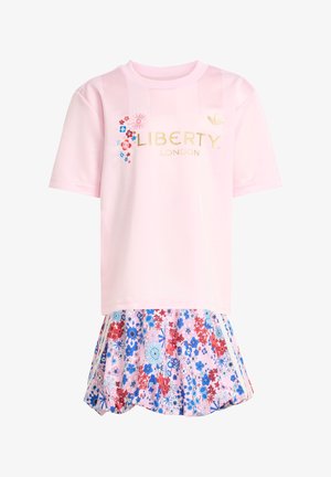 Vaaleanpunainen lyhythihainen paita, jossa kultaiset tekstit "LIBERTY LONDON"; kukkakuvioinen liehuva hame punaisen, sinisen ja vaaleanpunaisen sävyissä.