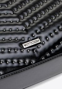 Borsa a mano in pelle nera con superficie testurizzata caratterizzata da borchie in rilievo. È visibile una targhetta con logo argentata. Finitura liscia e lucida. Forma rettangolare.