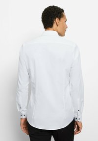 White long-sleeve shirt with a smooth texture, a classic collar, and black cuff buttons, viewed from the back. Slightly tailored fit.