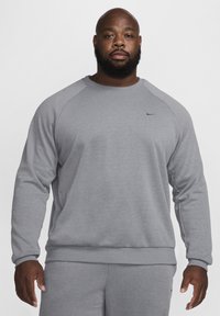 Szary sweatshirt z rękawami raglanowymi, okrągłym dekoltem, miękką teksturą i subtelnym logo Nike na piersi, w komplecie ze spodniami w tym samym kolorze.