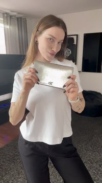 Portafoglio in pelle argento con una texture liscia e finitura metallica. Presenta un logo ed è tenuto da una persona che indossa una maglietta bianca.