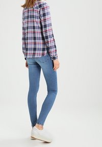 Rutig skjorta i marinblått, rött och vitt; lättviktsmaterial. Kombinerad med blå skinny jeans och vita sneakers med en beige sula.