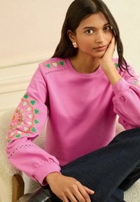 Roze sweatshirt met geborduurde, meerkleurige hartjes op de mouwen, gemaakt van zachte stof, met een ronde hals en geplooide manchetten.