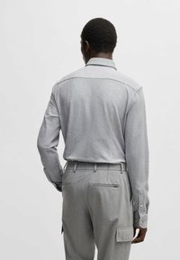 Grijze lange mouwen shirt met een kraag, zachte textuur en knoopmanchetten, gecombineerd met lichtgrijze broek met cargozakken.
