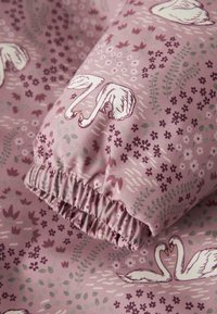 Mønstret stoff med svaner og blomster i nyanser av rosa og lilla, med rynket kant for elastisitet. Myk, tekstilaktig tekstur.