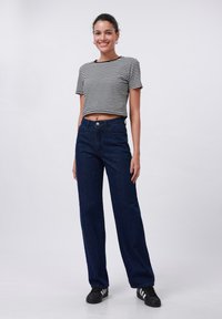 Wzorzysty, krótki t-shirt w czarno-białe paski, dopasowany do spodni z wysokim stanem, szerokich w nogawkach z ciemnego dżinsu. Czarne trampki z trzema białymi paskami.