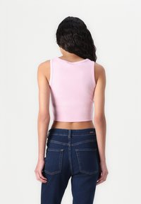 Roze rebrasti kratki top s širokim trakama, uparen s tamnoplavim trapericama visokog struka koje imaju dva stražnja džepa i detalje šivenja.