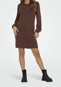 Abito lavorato a maglia color ruggine con maniche a sbuffo lunghe, scollatura rotonda e vestibilità comoda, abbinato a stivaletti neri alla caviglia.