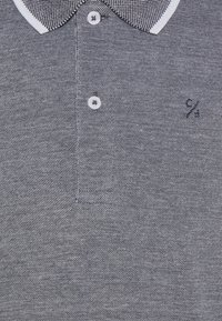 Pikéhemd med en teksturert grå stoff, med en houndstooth-mønsteret krage, tre hvite knapper og en liten marineblå logo på brystet.