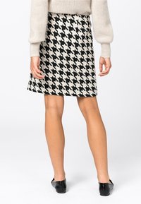 Valkoinen ja musta houndstooth-kuvioinen hame, jossa on tiivis muotoilu, polvipituinen leikkaus ja sileä pinta. Yhdistetty yksinkertaisiin mustiin kenkiin.