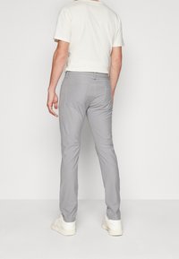 Pantaloni grigi leggeri con una vestibilità slim, dotati di due tasche posteriori e dettagli di cucitura sottili, abbinati a una t-shirt crema e sneakers bianche.