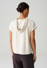 Top a maniche corte di un beige chiaro con cappuccio drappeggiato, texture liscia e un semplice design della cucitura posteriore, abbinato a pantaloni scuri.
