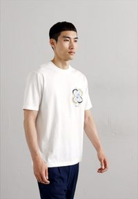 Hvid bomulds T-shirt med et flerfarvet blomstermotiv på brystet, korte ærmer og rund hals.